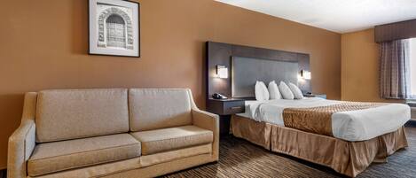A hotel room with a sofa, a bed with a headboard, a framed picture on the wall, and a carpeted floor.