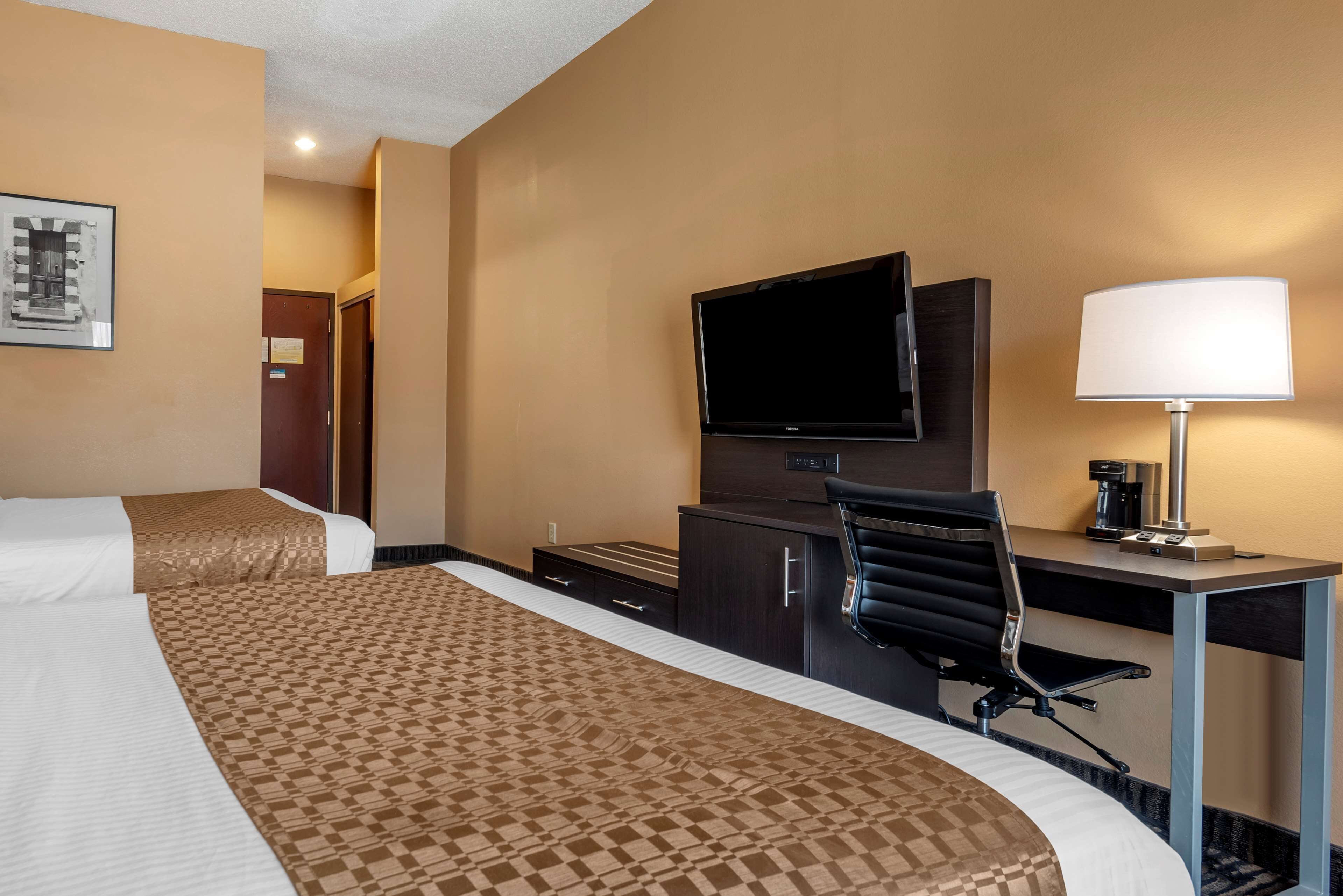 A hotel room with two beds, a desk, a chair, a television, and a lamp.
