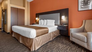 A hotel room with a large bed, a nightstand with a lamp, a chair, and a wardrobe.