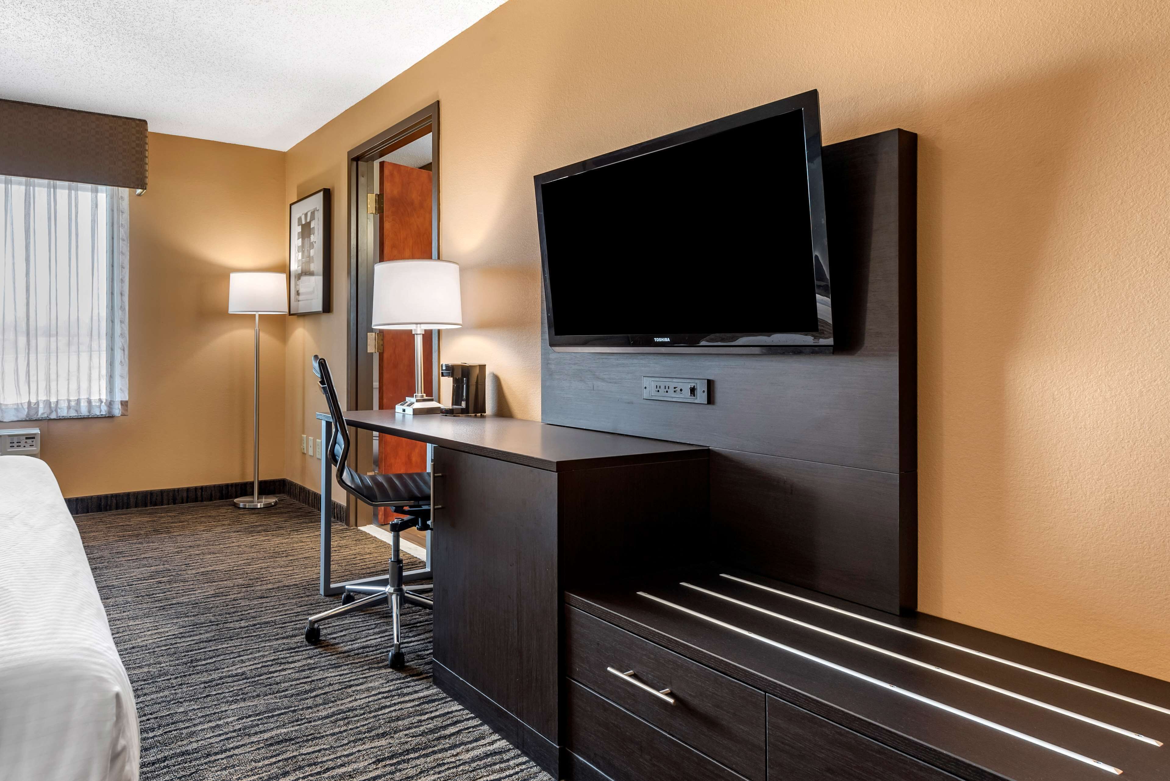 Une chambre d’hôtel équipée d’un lit, d’un bureau, d’une chaise, d’une télévision, d’une lampe et d’un grand miroir.