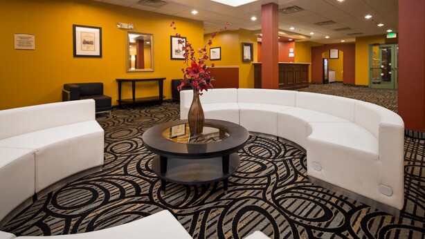 A lobby with a white curved sofa, a round table with a vase, patterned carpet, and framed pictures on the walls.