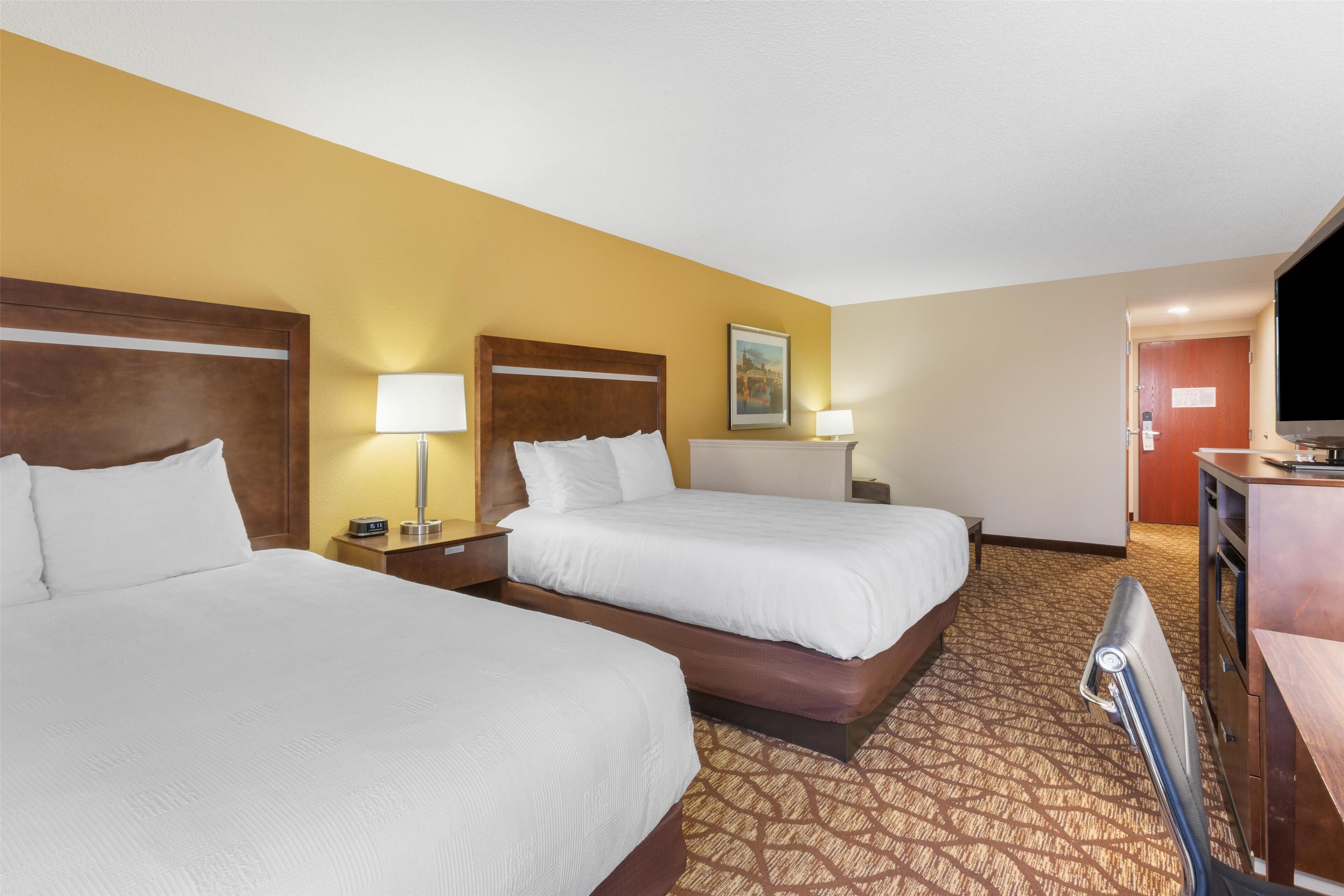 A hotel room with two beds, a wooden headboard, bedside lamps, a flat-screen TV, and a carpeted floor.