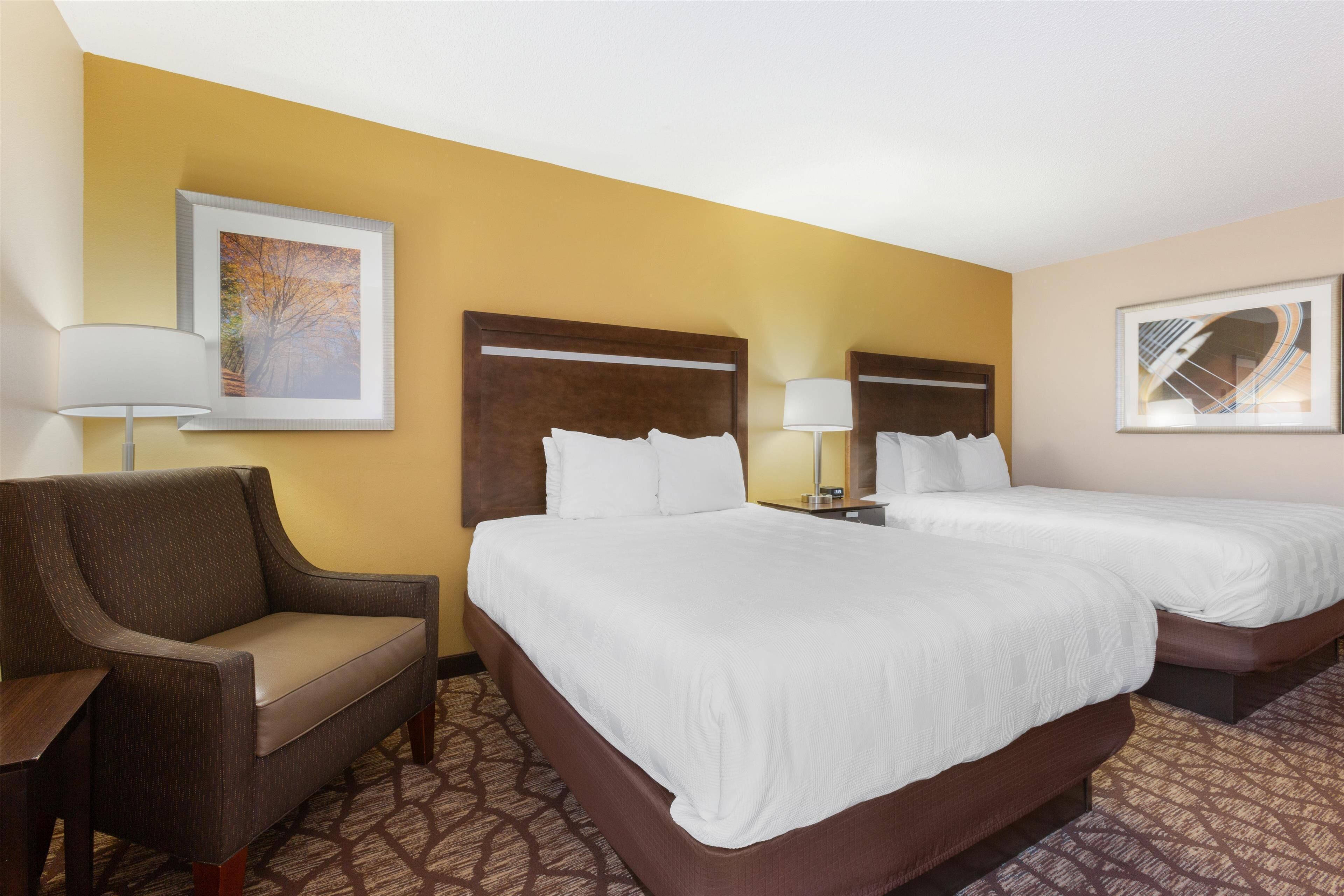 A hotel room with two beds, a sofa, and a nightstand with lamps.