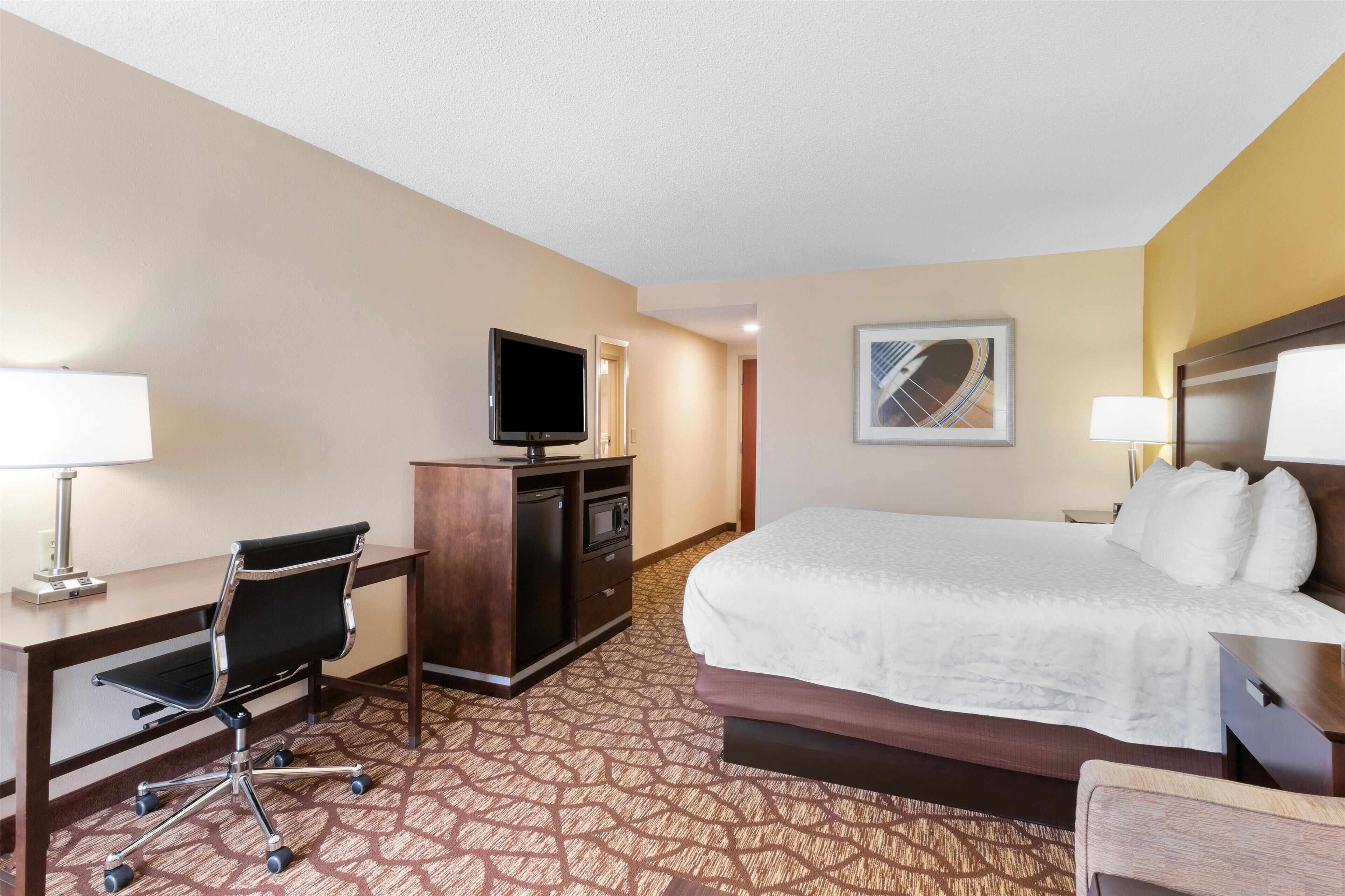A hotel room with a bed, desk, chair, TV, and a carpeted floor.
