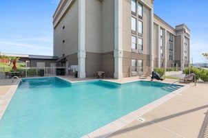 A swimming pool with lounge chairs and tables, surrounded by a building with large windows and a view of the city.