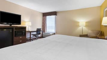 A hotel room with a large bed, a desk with a chair, a television, a microwave, and two lamps.