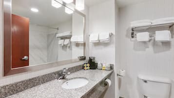 A bathroom with a granite countertop sink, a mirror, a toilet, and a towel rack with folded towels.