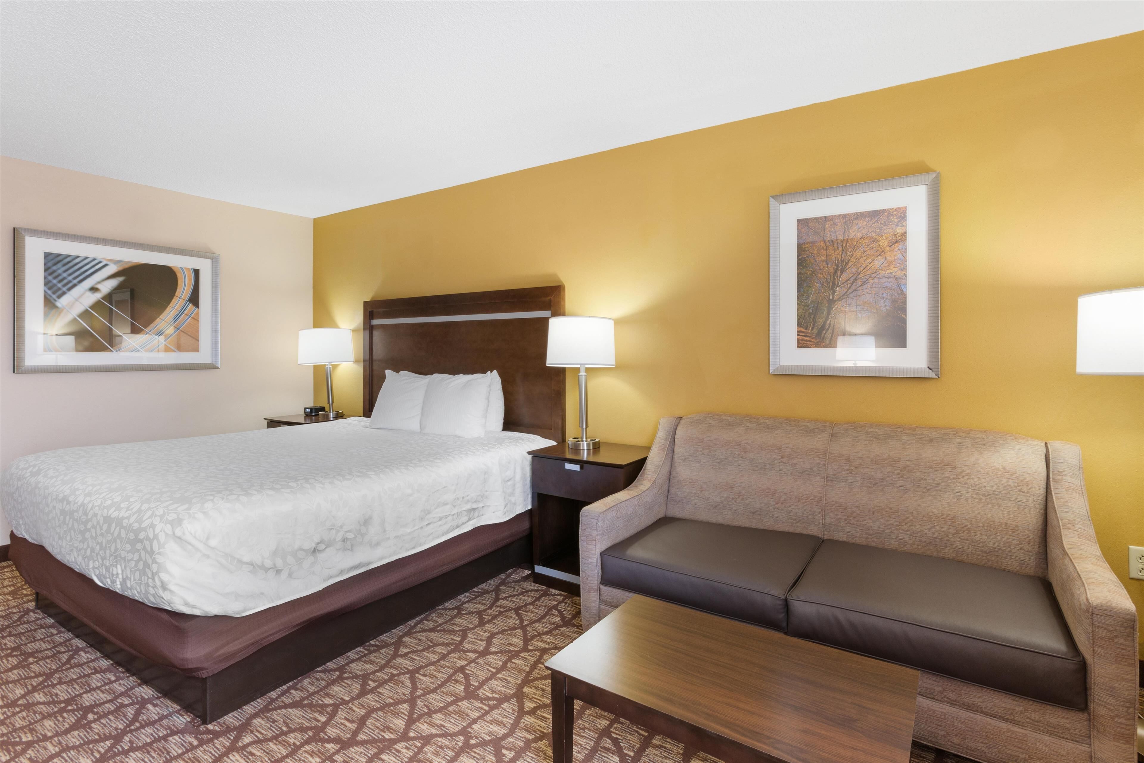A hotel room with a bed, a sofa, a coffee table, and two lamps.