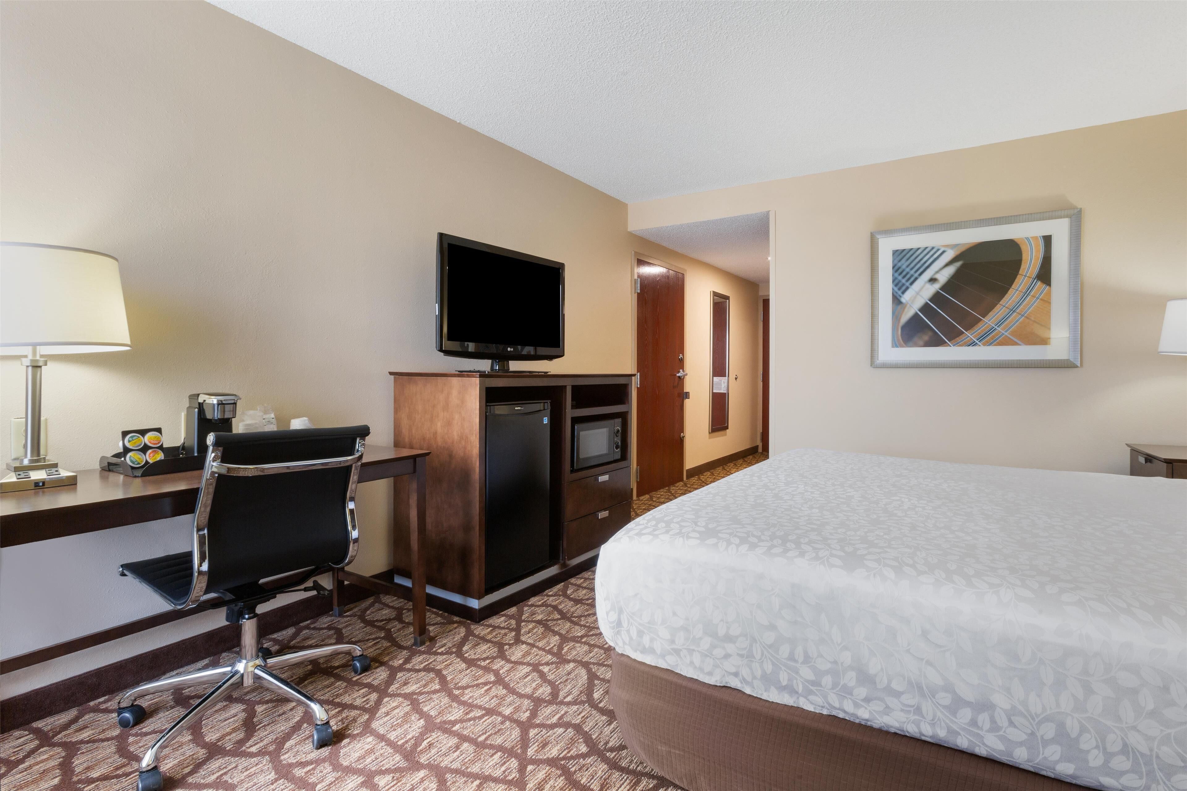 A hotel room with a bed, desk, chair, television, microwave, and refrigerator.