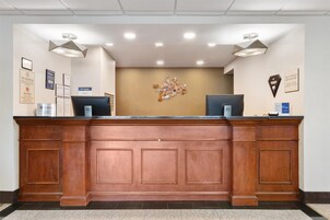 A reception desk with a wooden finish, two computer monitors, and a wall-mounted light fixture.