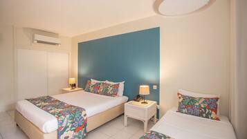 Une chambre d’hôtel avec deux lits, une table de chevet avec une lampe, un appareil de climatisation et un mur d’accent bleu.