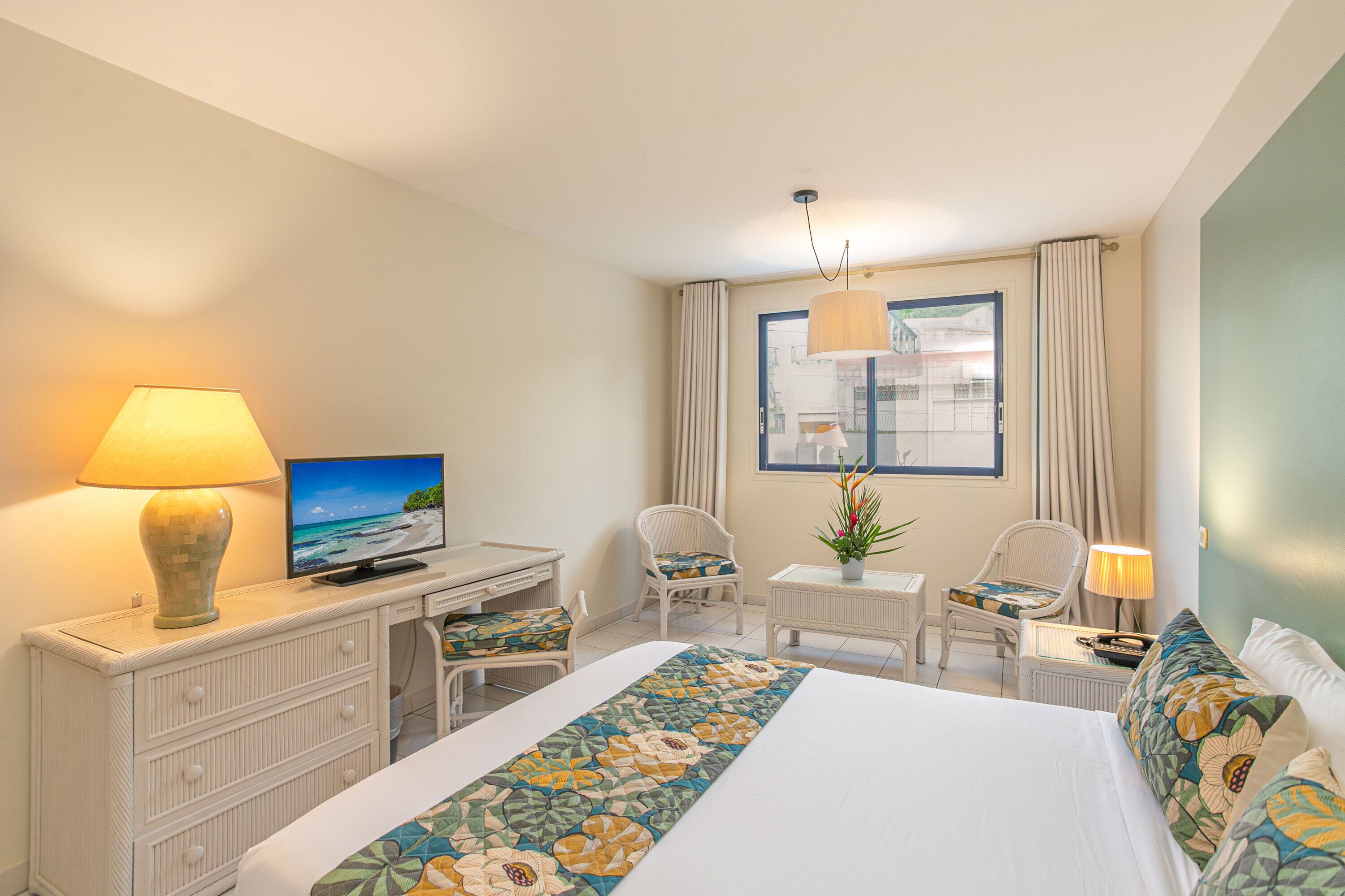 A hotel room with a bed, a desk, a chair, a TV, and a window with curtains.