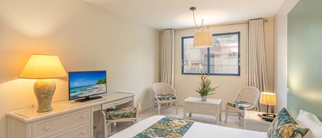 A hotel room with a bed, a desk, a chair, a TV, and a window with curtains.