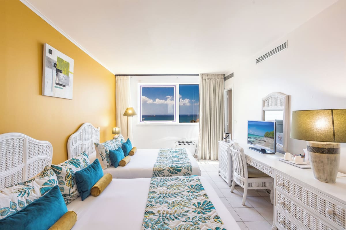 A hotel room with two beds, a desk, a TV, and a window with a view.