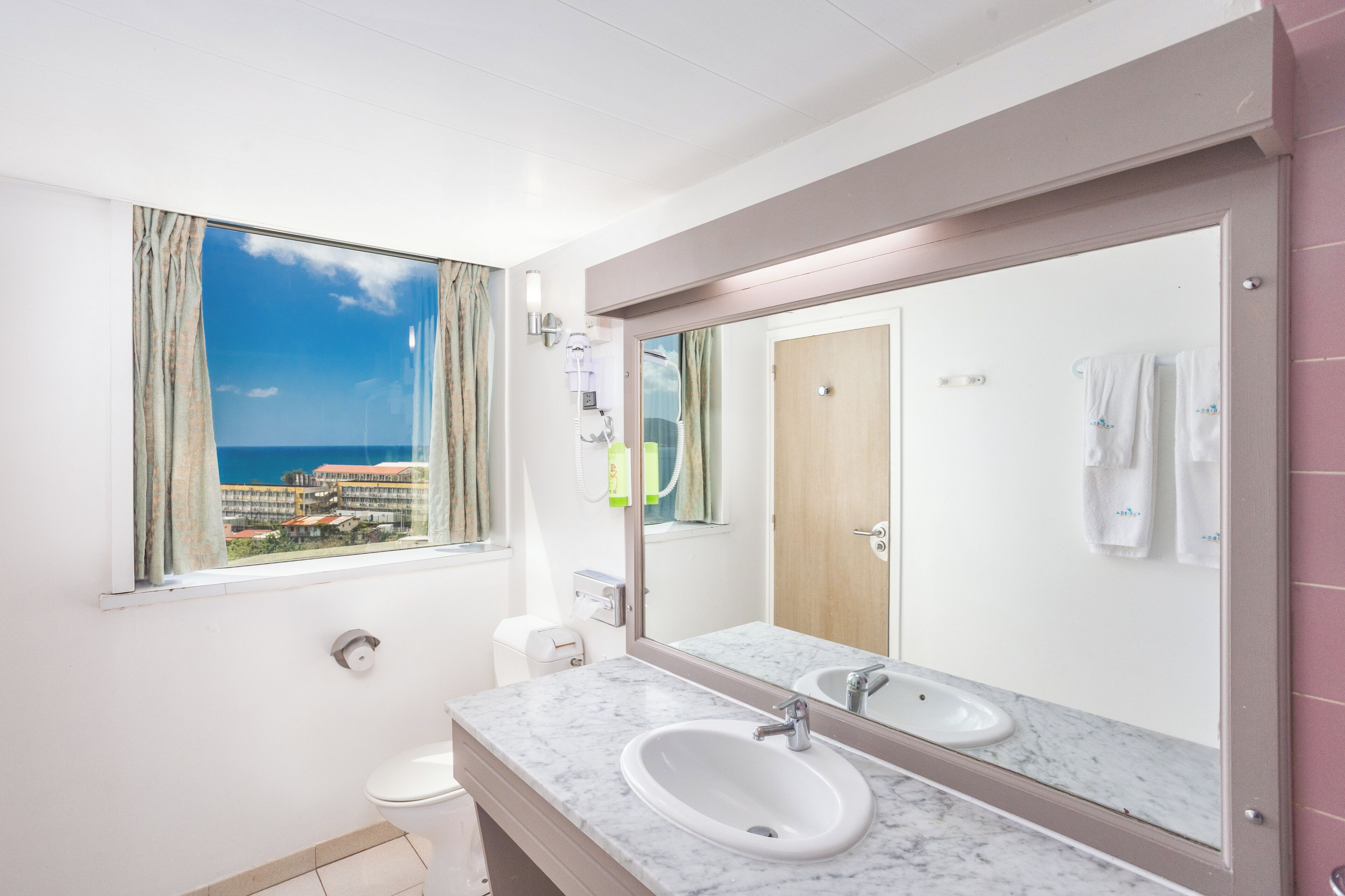 Un baño con un ventanal grande, un lavabo de mármol, un espejo y vista al mar.