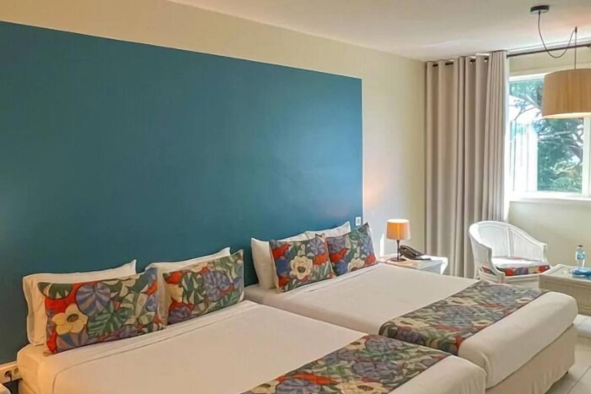 A hotel room with two beds, a nightstand, a chair, a lamp, and a window with curtains.