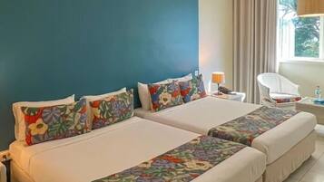 A hotel room with two beds, a nightstand, a chair, a lamp, and a window with curtains.