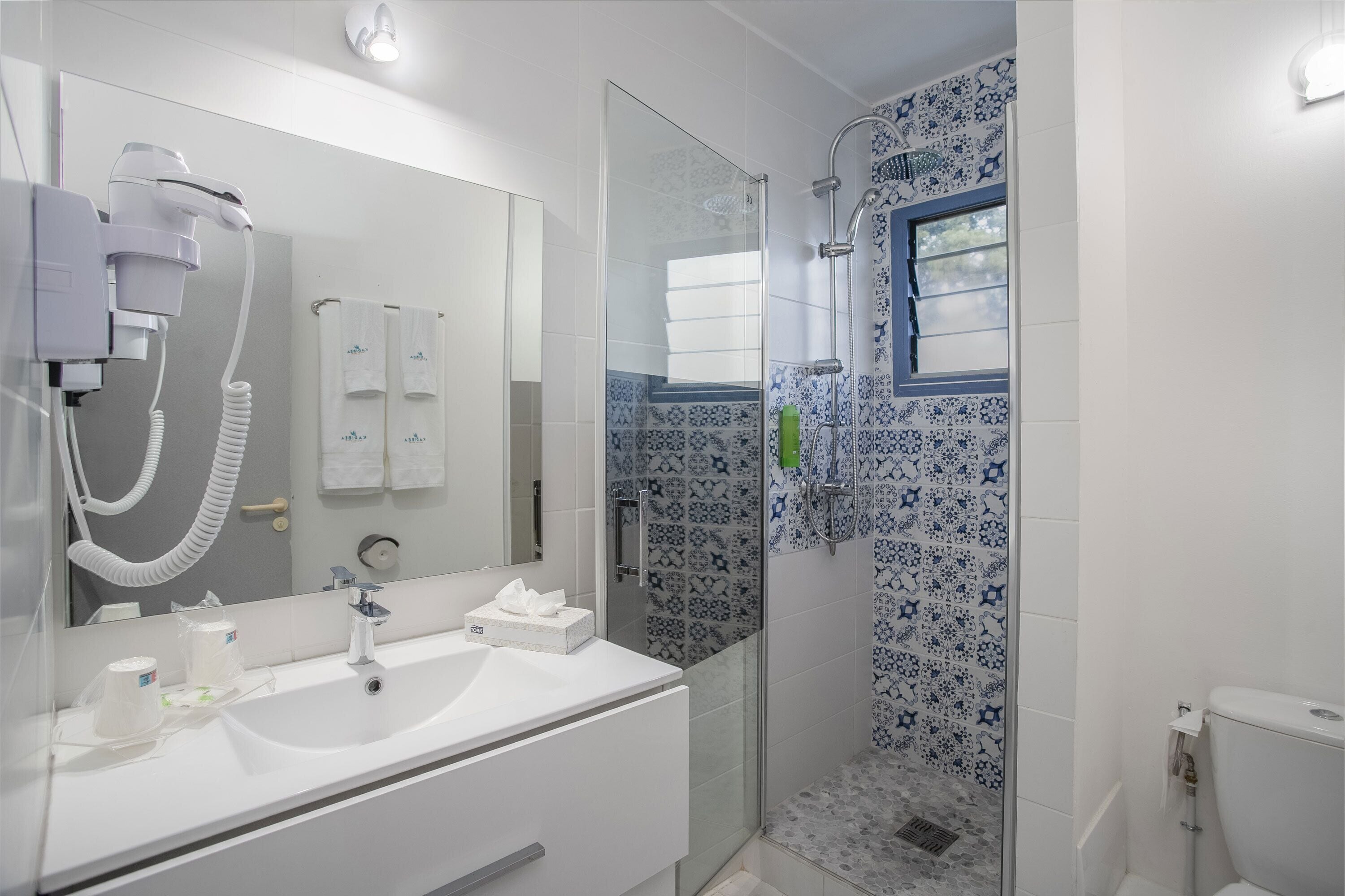 Un baño moderno con un lavamanos blanco, un secador de pelo y una ducha con azulejos estampados.