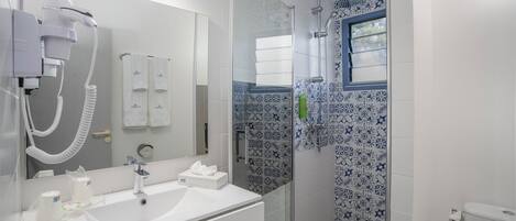 Un baño moderno con un lavamanos blanco, un secador de pelo y una ducha con azulejos estampados.