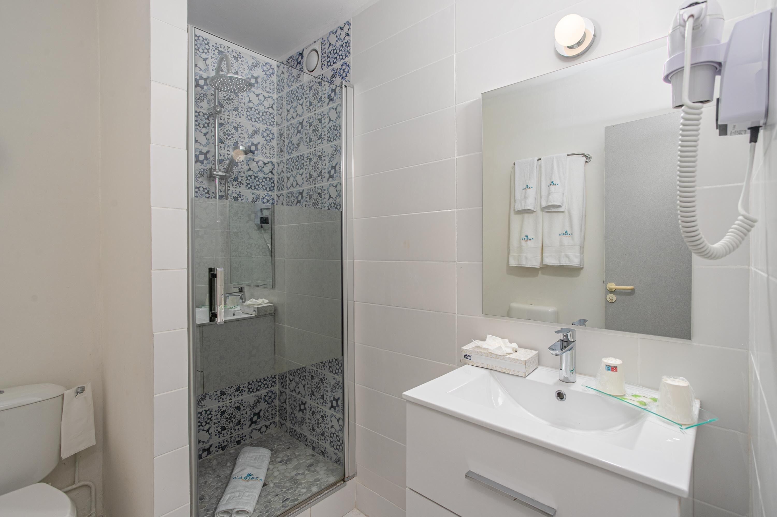 Un baño con ducha, inodoro, lavabo y secador de pelo montado en la pared.