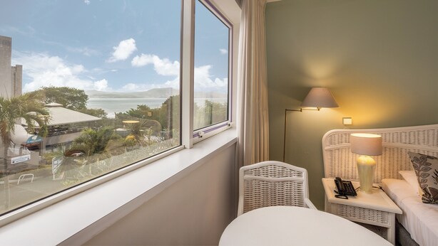 A hotel room with a large window, a bed, a bedside table with a lamp, and a chair.