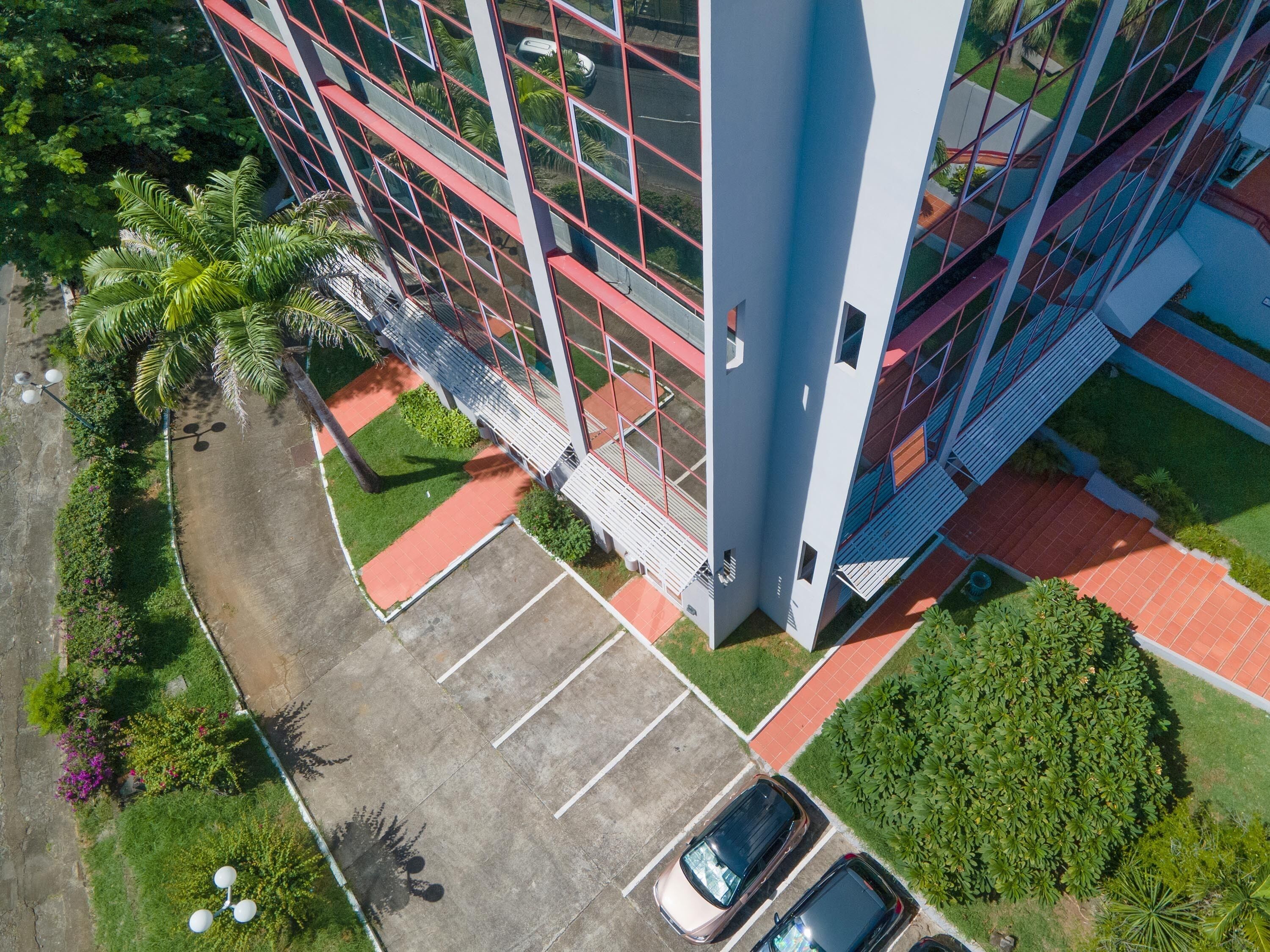 Vista aérea de un edificio moderno con estacionamiento, áreas verdes y dos coches aparcados.
