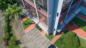 Vista aérea de un edificio moderno con estacionamiento, áreas verdes y dos coches aparcados.