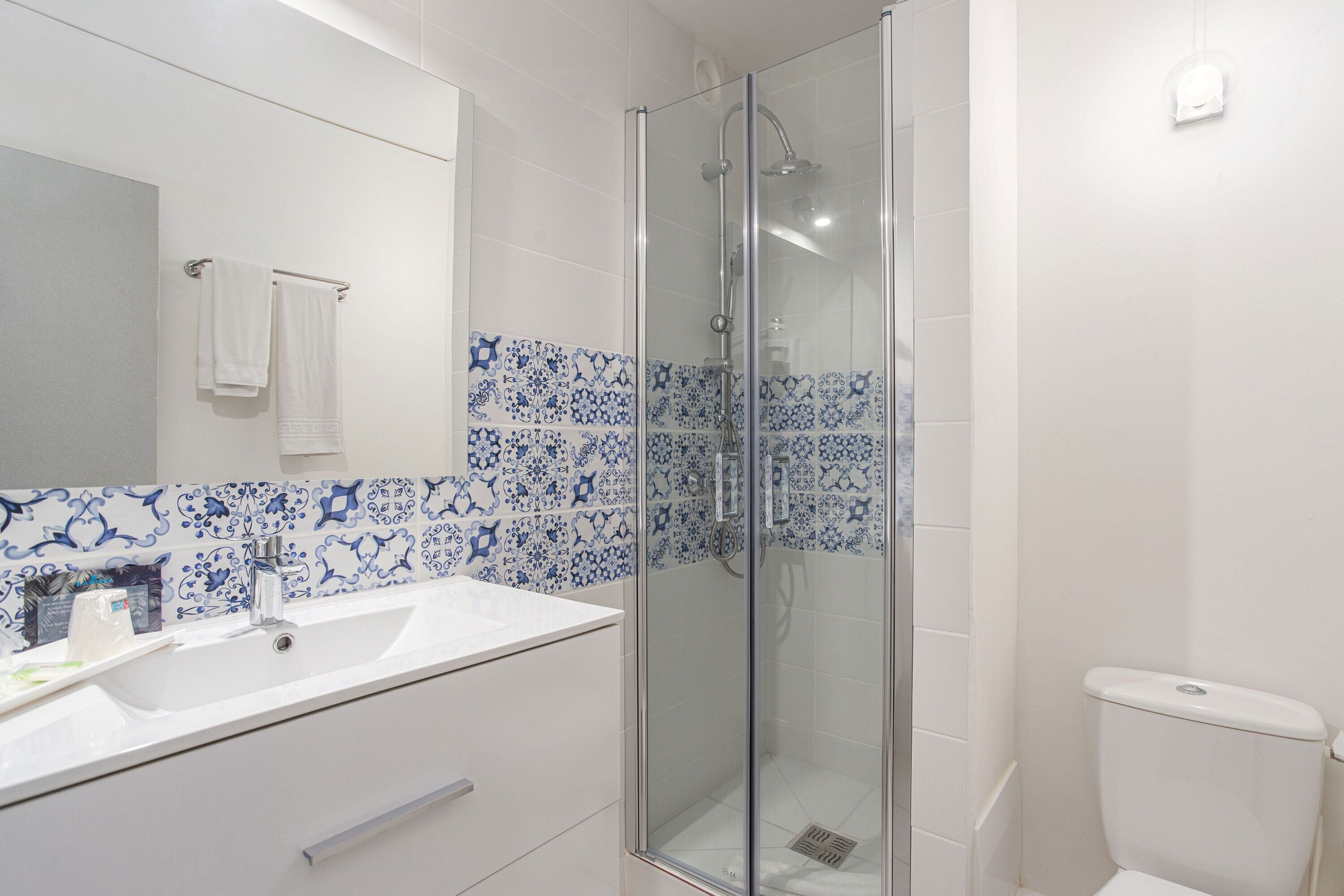Une salle de bain avec une douche à parois de verre, un lavabo blanc et des carreaux bleus à motifs.
