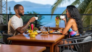 A couple dining at an outdoor table with a view of the ocean and mountains. - Karibea Squash Hôtel (Fort-de-France)