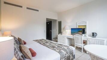 A hotel room with a bed, a desk, a chair, a lamp, a painting, and a kettle.