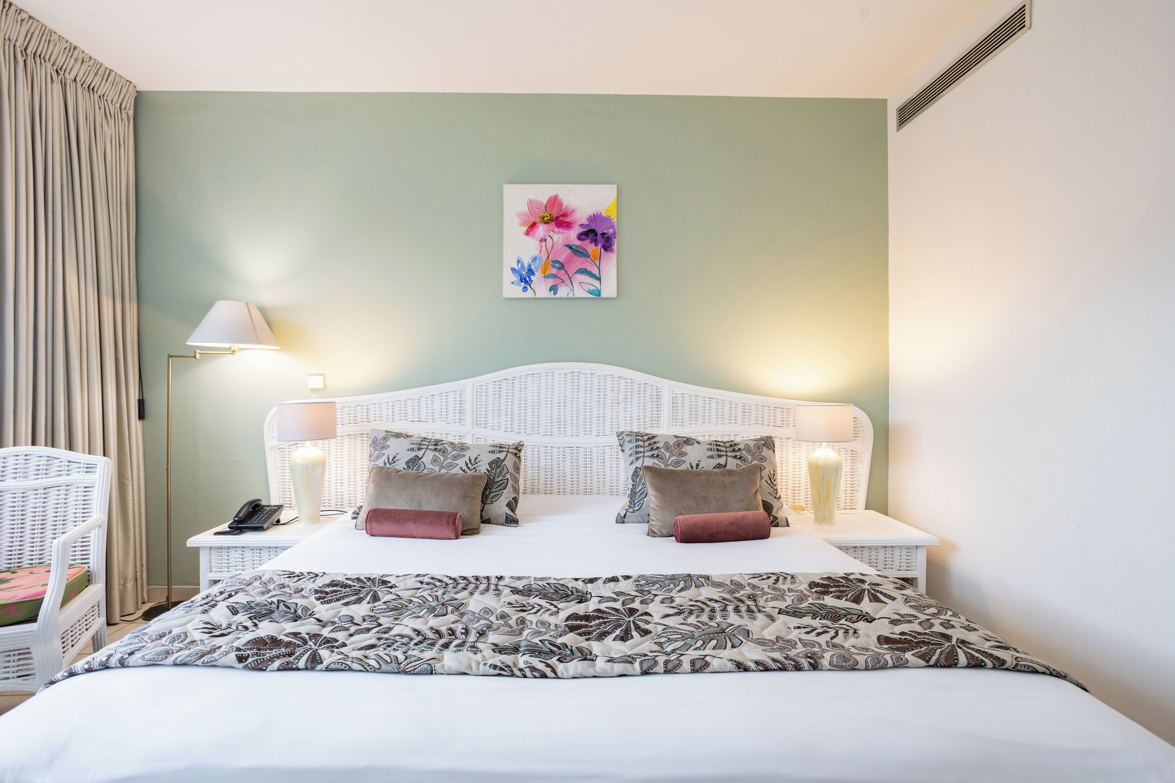 Una camera d'albergo con un letto, due comodini, una lampada, un quadro e una sedia.