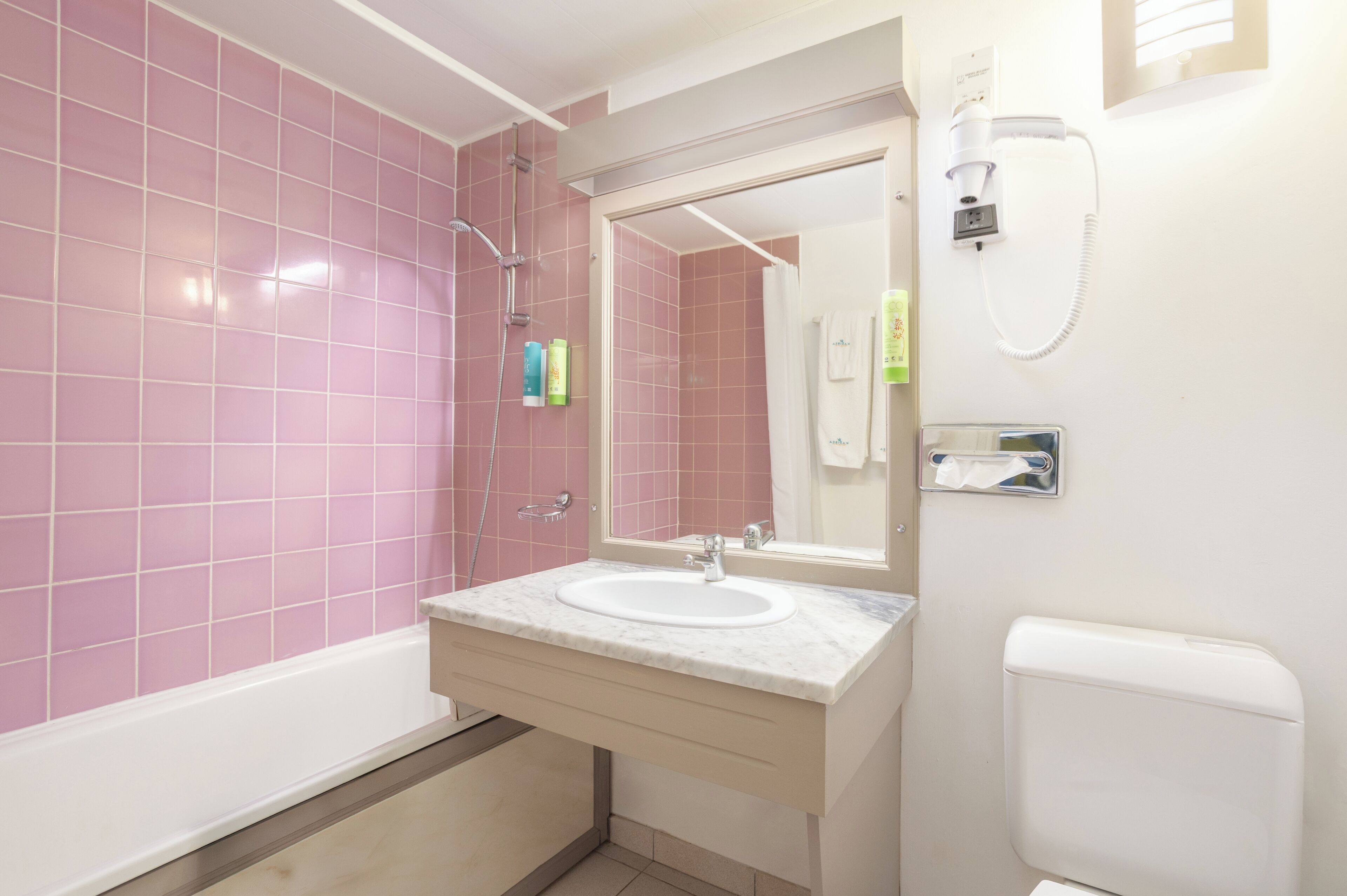 Un baño con azulejos rosas, un lavamanos blanco, un espejo, una ducha y un inodoro.