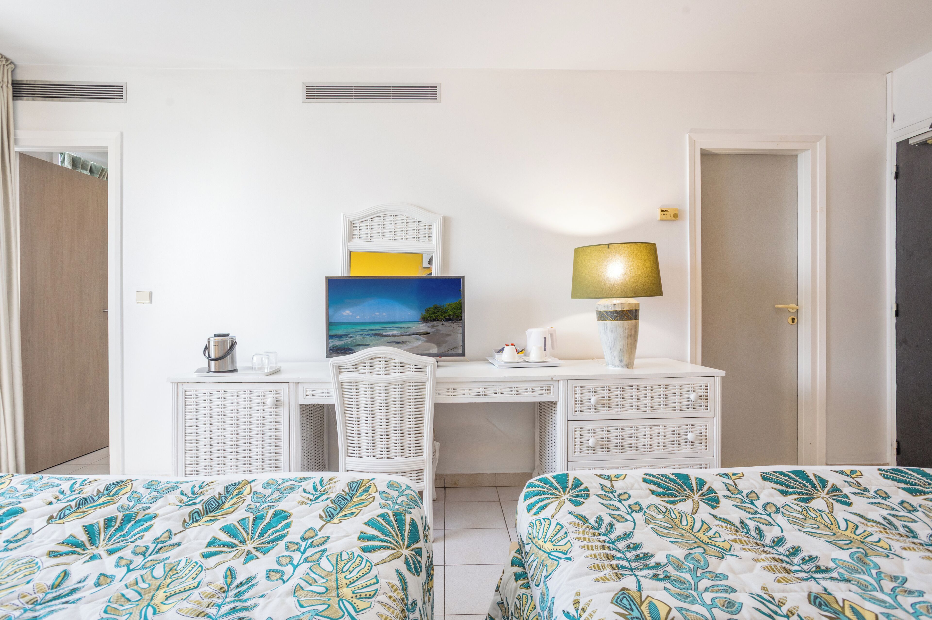 A hotel room with two beds, a desk, a chair, a lamp, a painting, and a wardrobe.