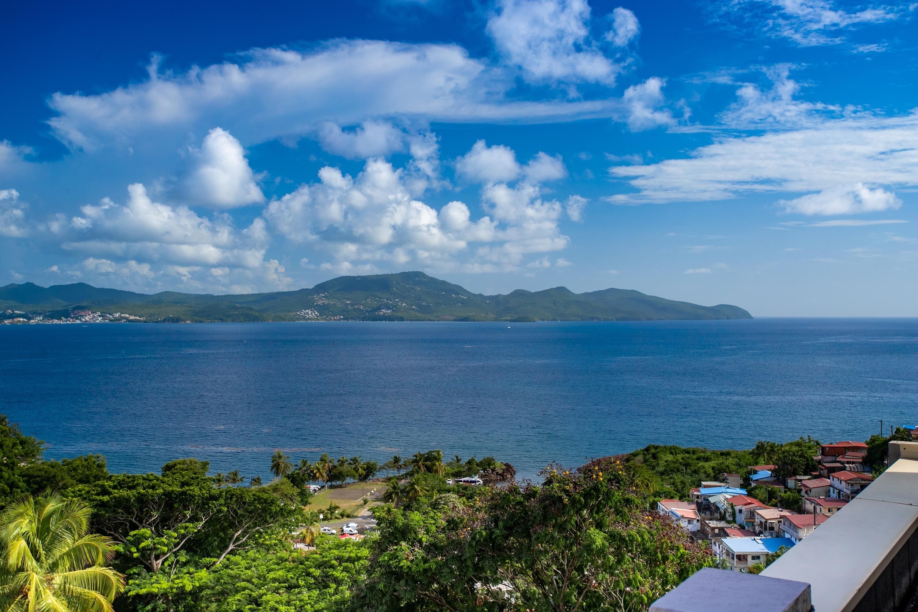 A coastal view with a clear sky, a calm sea, and a small settlement with colorful buildings.
