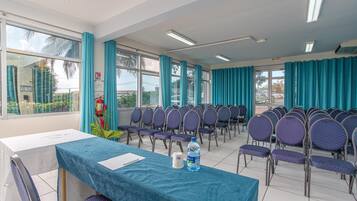 Une salle de conférence avec des rangées de chaises, une table recouverte d’une nappe bleue et une bouteille d’eau posée sur la table.
