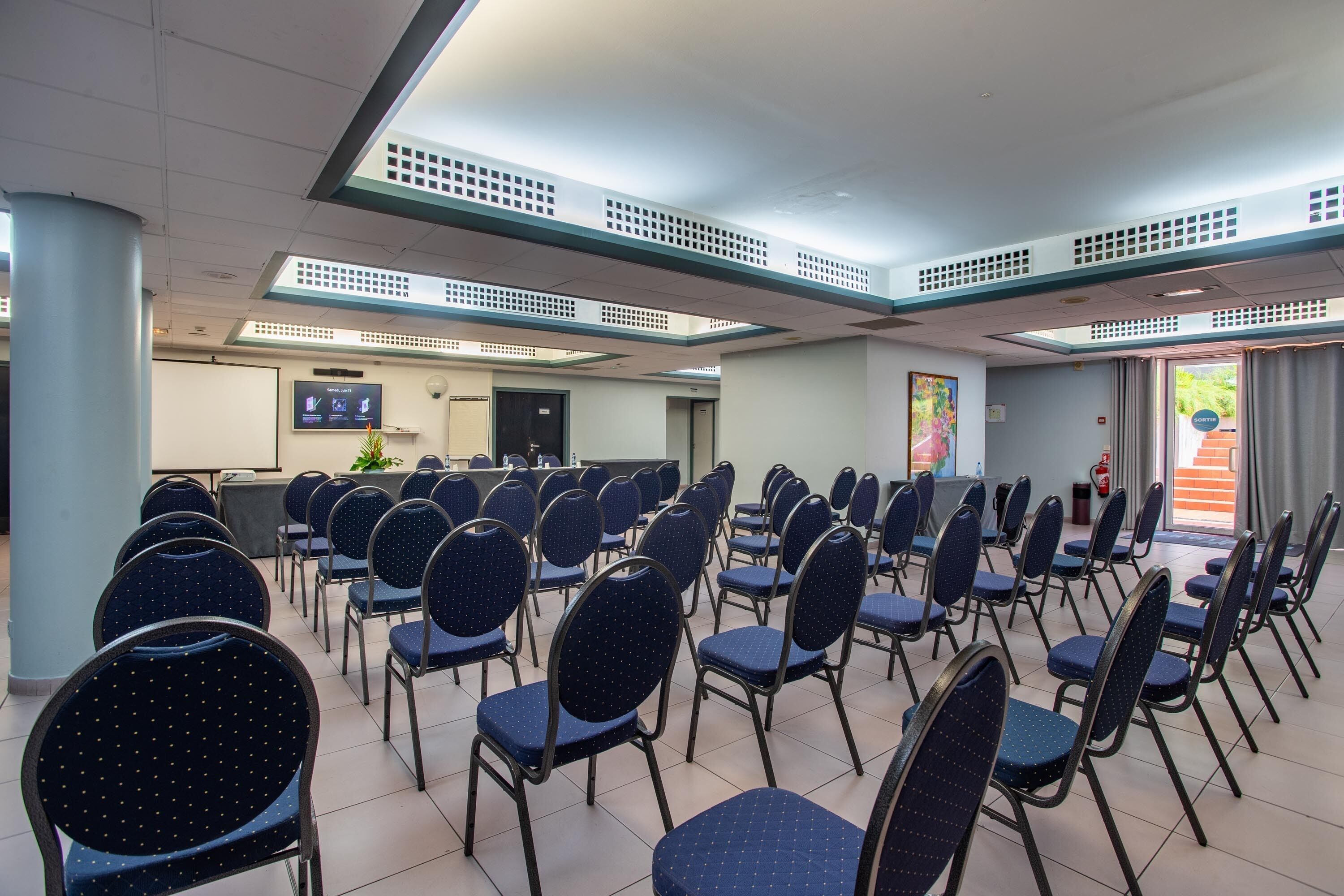 A conference room with rows of foldable chairs, a projection screen, and a reception desk.