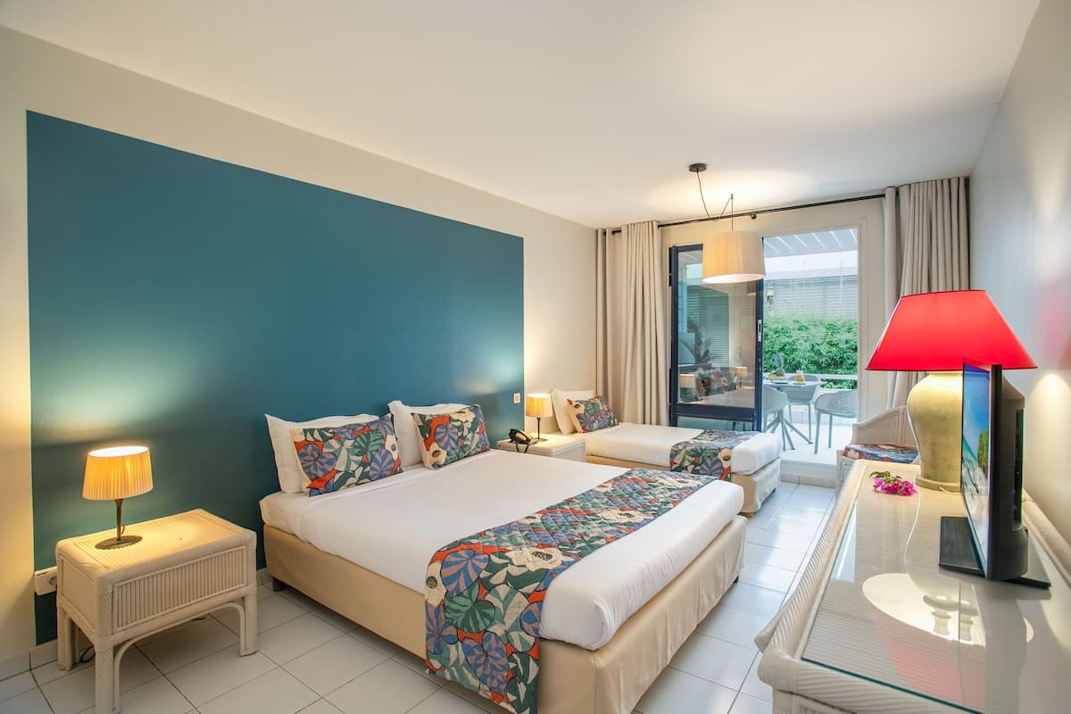 A hotel room with two beds, a glass table, a TV, and a balcony with a view.