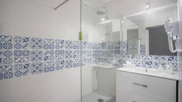 Un baño con cabina de ducha de vidrio, azulejos blancos con motivos florales azules, un lavabo blanco y un espejo con secador de pelo.