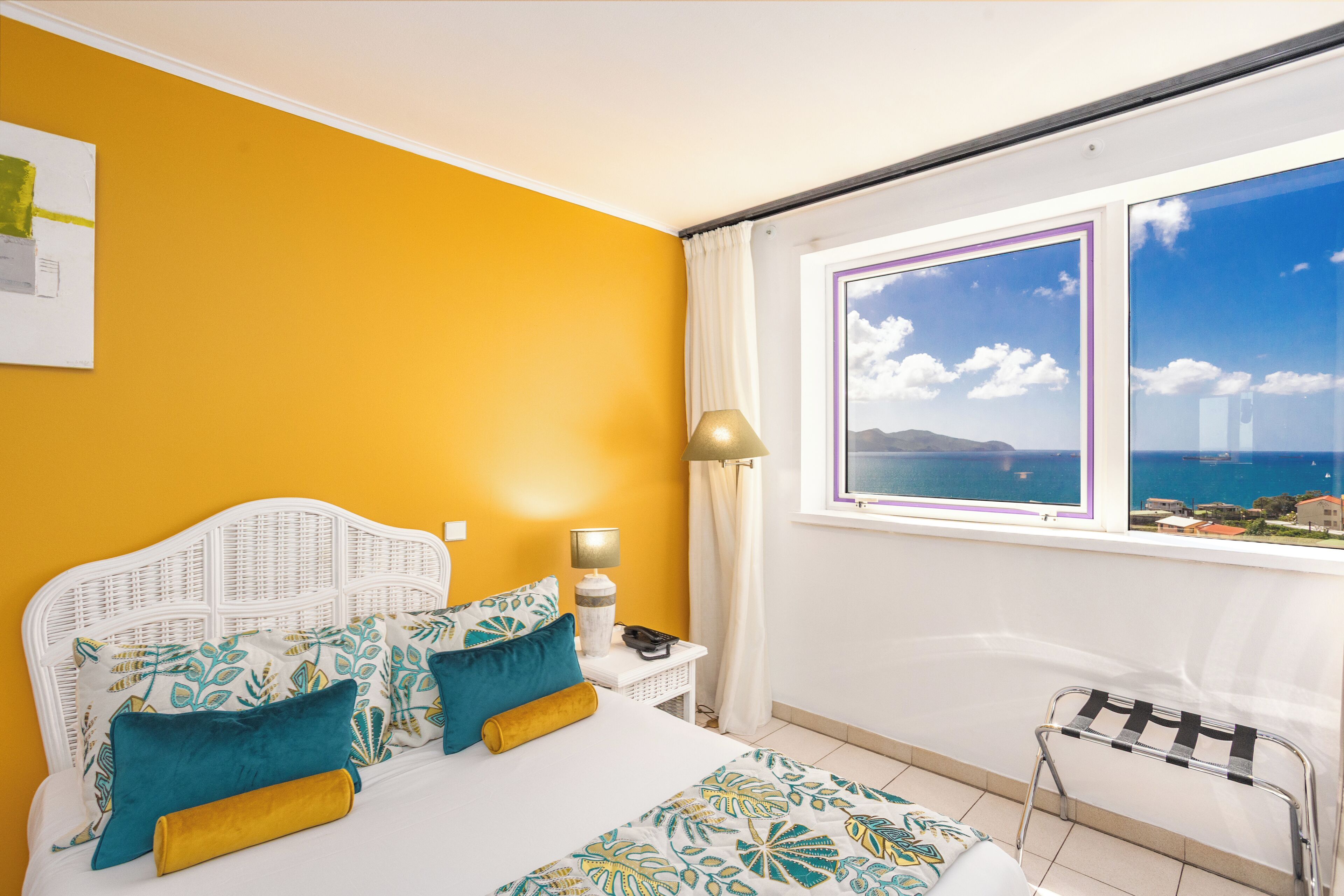 Una camera da letto con un letto, un comodino, una lampada, una sedia e una finestra vista mare.
