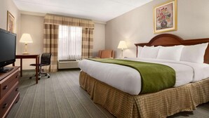 A hotel room with a large bed, a desk with a lamp, a chair, and a television.