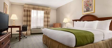 A hotel room with a large bed, a desk with a lamp, a chair, and a television.