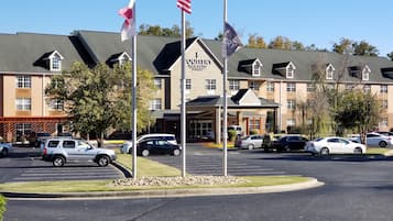 Un hotel con entrada principal, varias banderas y un estacionamiento con varios coches.