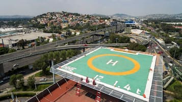 A helipad with a green surface and a white 'H' in the center, surrounded by a metal safety fence.