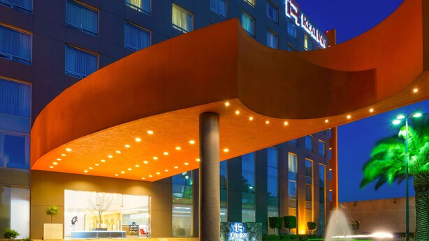 A hotel entrance with a curved awning, a fountain, and a well-lit building facade. - Real Inn Perinorte (Tlalnepantla de Baz)
