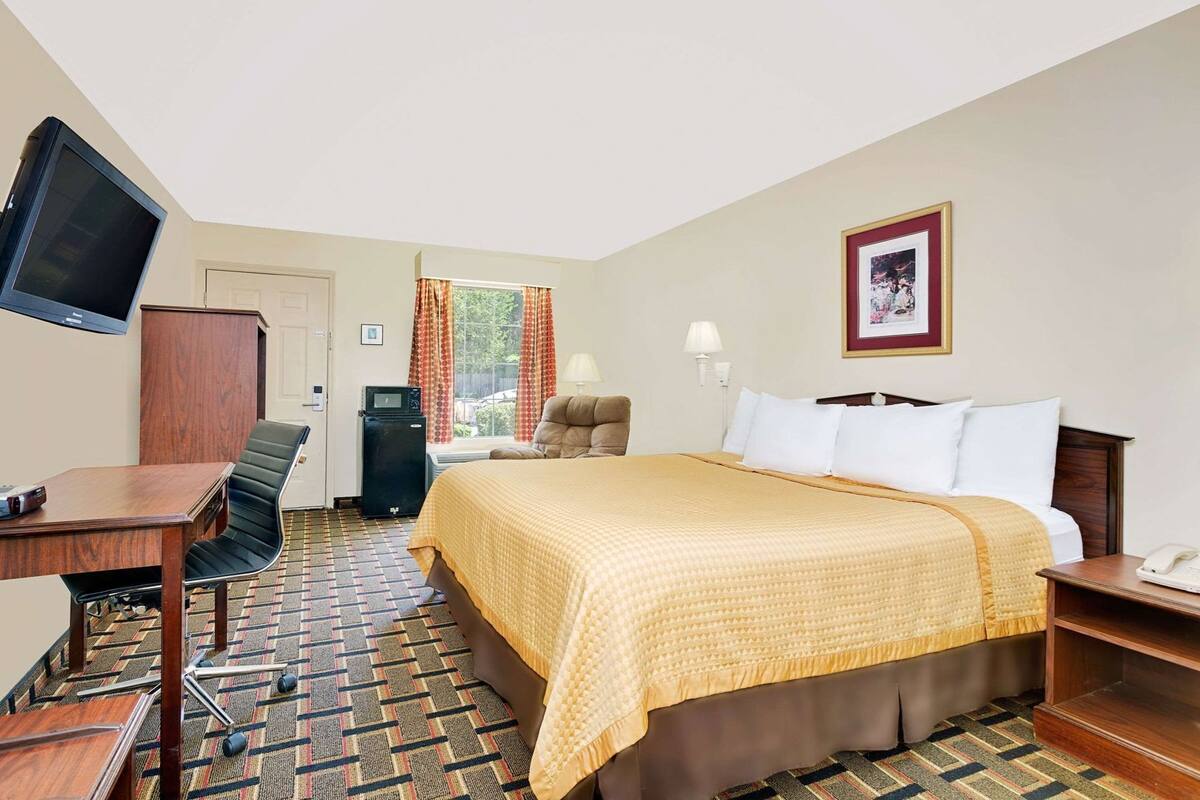 A hotel room with a bed, desk, chair, television, and a window with curtains.