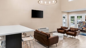 Un hall d’entrée moderne avec un grand comptoir de réception blanc, des canapés en cuir marron, une table basse ronde et un luminaire suspendu au plafond.
