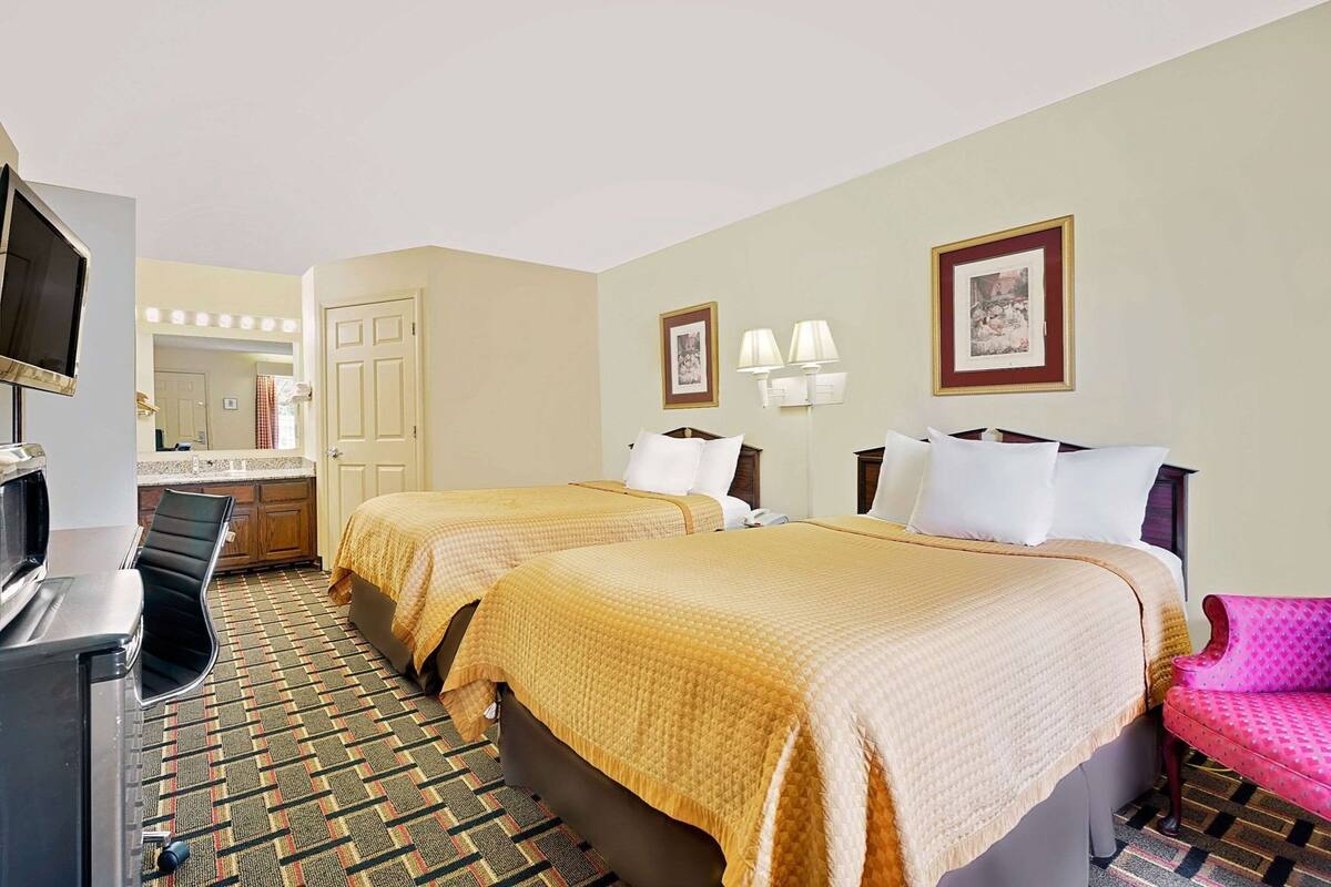 A hotel room with two beds, a desk, a chair, a TV, and a mirror.