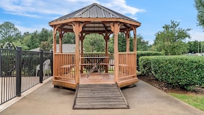 Un kiosque en bois avec un toit en métal, un banc et une rampe menant à l’intérieur.