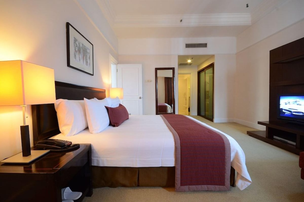 Une chambre d’hôtel comprenant un lit, des lampes de chevet, une télévision, un bureau et une porte donnant sur une autre pièce.