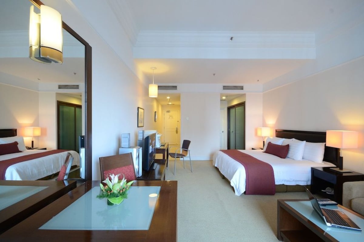 Une chambre d’hôtel avec deux lits, un bureau avec une chaise, une table basse et un téléviseur.